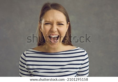 Close up studio shot of a crazy stressed beautiful young woman with an angry displeased face expression screaming loudly at the camera. Portrait of a mad girlfriend or enraged school teacher Royalty-Free Stock Photo #2101295158