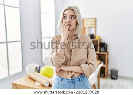 Young beautiful caucasian woman at construction office looking stressed and nervous with hands on mouth biting nails. anxiety problem.  Royalty-Free Stock Photo #2101299028