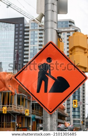 Construction orange sign near construction site against tall buildings and sky