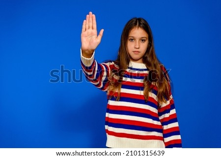 Pretty Hispanic girl making the gesture of stopping with the palm of her hand isolated on a blue studio background, faces with determination and courage the possible dangers that she may face.