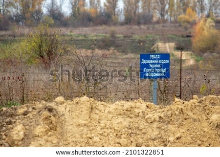 Inscription "Attention! State border of Ukraine. Passage prohibited" on a blue plate on an iron mesh fence rewound with barbed wire. Closed area. Border protection and illegal migration concept