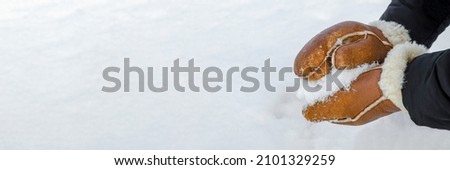 First snow, making snowballs in the park close-up. Hands in warm mittens make snow in winter. Brown leather mittens in the snow in winter.