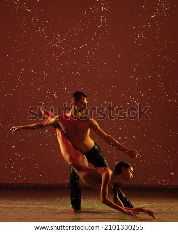 Art and love. Two ballet dancers, young man and woman in art performance dancing under the rain over red background. Concept of human emotions and feelings, relationship, art and theater.
