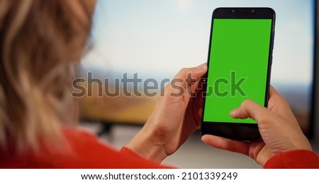 Woman at Home Sitting on a Couch using Smartphone with Green Mock-up Screen, Doing Swiping, Scrolling Gestures. Girl Using Mobile Phone, Internet Social Networks Browsing.