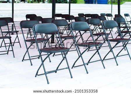 folding black chairs stand in a row on a white wooden floor outside Royalty-Free Stock Photo #2101353358