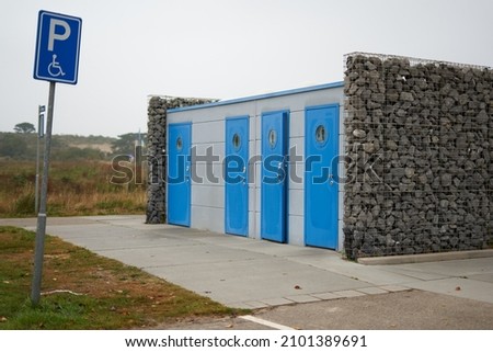 Public toilets with 4 blue doors in front of a handicapped parking space. Building is located between 2 gabions. Netherlands, Renesse.
