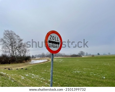 Road sign indicating customs, Zoll, douane, between border of Austria and Liechtenstein, in green landscape against blue sky.