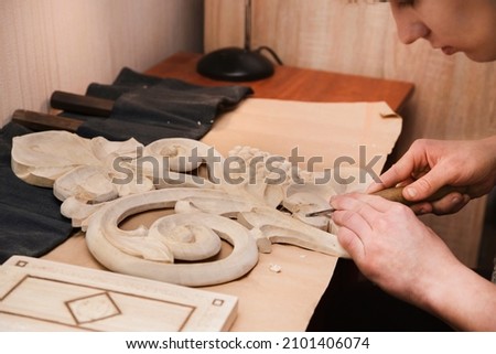 The teenage boy enthusiastically works with a tree at home - he cuts a wall decoration with elements of a vine with a special knife from a glued tree. Because of hobby, the guy is not depressed