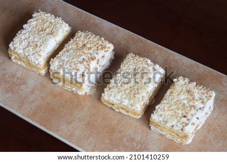 Several individual servings of Crusted in a row on an abstract textured, pastel-colored tray. Traditional sweet puff pastry dessert with cream and meringue covered with chopped almonds and icing sugar