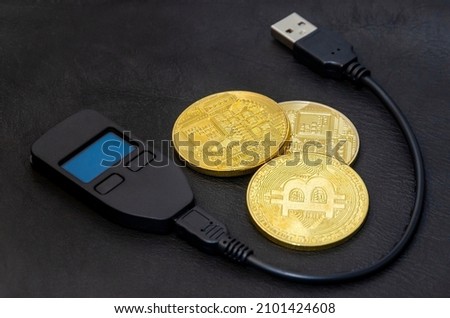 Gold bitcoins (physical symbol of bitcoins) with a hardware crypto wallet on a dark black leather background. The concept of saving cryptocurrencies.
