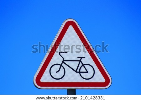 A red and white road sign of a triangular shaped bicycle path with an image of a bicycle on a blue sky background.