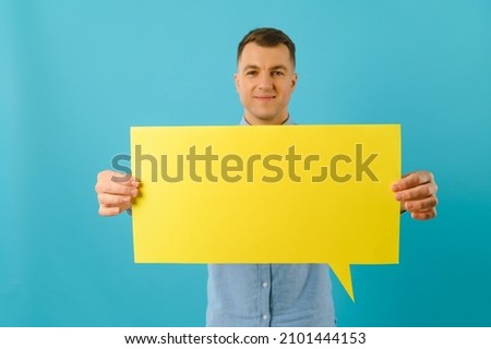 Joyful Caucasian man demonstrating blank placard on blue studio background, mockup for design