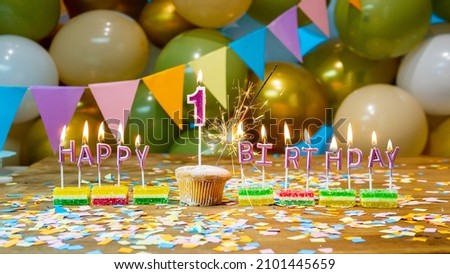 Happy birthday greeting card to 1 year old child, birthday cupcake with burning candles and birthday decorations on blue background