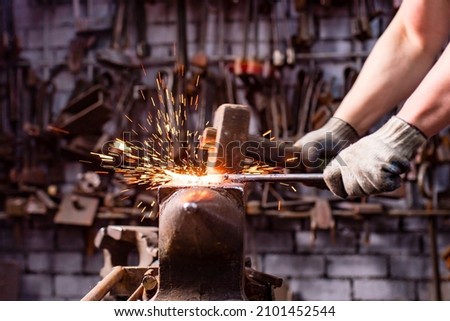 Authentic blacksmith man forges a metal product in dark indoors studio Royalty-Free Stock Photo #2101452544