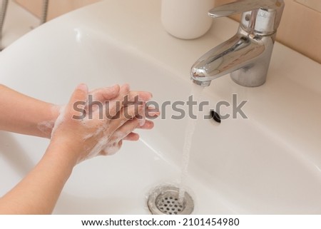 The hands of a young girl washing her hands with soap under the running water in the bathroom. Cleanliness and hygiene.