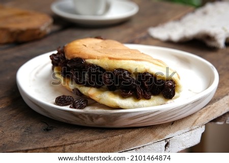 California Cake on a white plate, with a cup of coffee on a wooden table.  Fluffy cake with custard cream filling and raisins