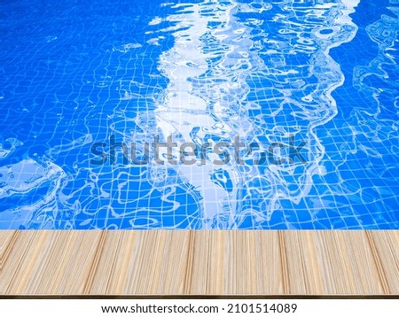 Artificial wooden tables in front, blue water waves in the swimming pool, and hotel reflections.