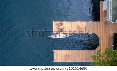 Summer aerial view of two Adirondack chairs on a wooden dock facing the blue water of a lake in Ontario. A yellow canoe is tied to the dock. Life jacket and oars are visible.  Royalty-Free Stock Photo #2101514680