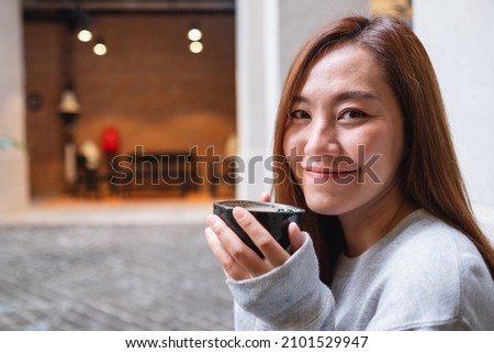 Portrait image of a young woman holding and drinking hot coffee