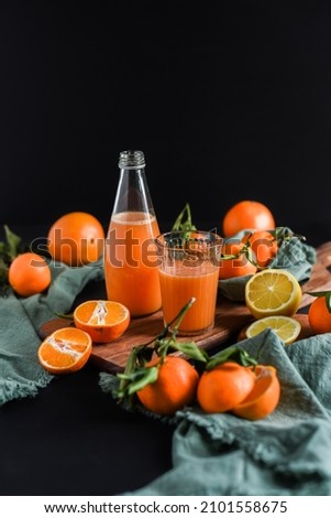 Freshly squeezed orange juice in a glass with citrus fruits on a dark background. Fruity still life on black background with fresh fruits