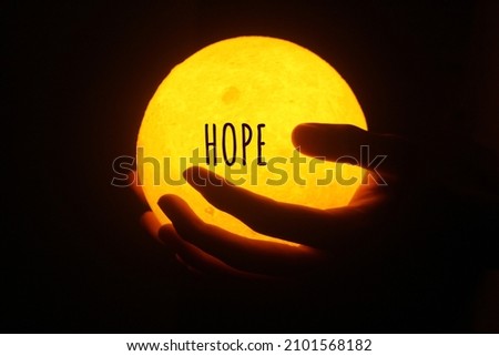 Person holding yellow ball lamp in hands with positive single word - HOPE, on dark background. Hope concept. Royalty-Free Stock Photo #2101568182