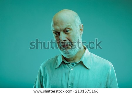 Sceptical senior man pulling a disbelieving face as he glances sideways with a dubious expression on blue Royalty-Free Stock Photo #2101575166