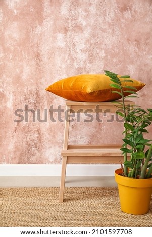Wooden step stool with pillow and houseplant near pink wall