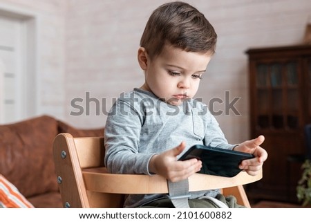 Cute little toddler boy playing with smartphone Healthy baby touching mobile phone with fingers, looking cartoons and having fun with educational apps. Child at home