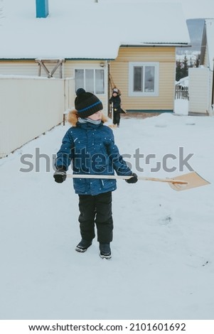 boy cleans snow with a shovel on the street. A boy clears the road from snow in winter. Hardworking child. A boy living in the village cleans the snow.