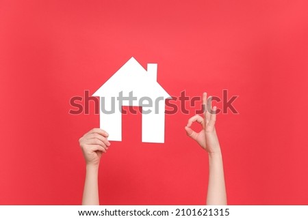 Female hands holding white house model and makes okay gesture, real estate home approval, isolated over red studio background wall with copy space for advertisement. Concept social service about home