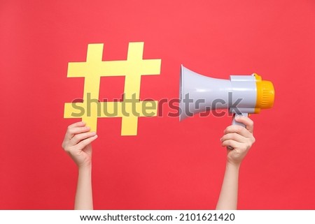 Close up female hands holding yellow hashtag sign and megaphone, label for business, marketing and advertising, isolated on red studio background. Concept social network monitoring, media measurement Royalty-Free Stock Photo #2101621420