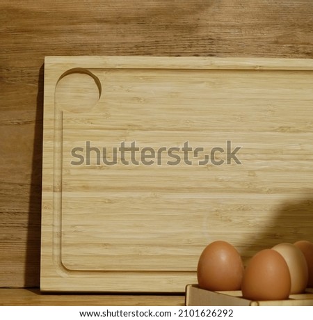 Modern composition on the kitchen interior with wooden cutting board,  eggs and kitchen accessories in wood  home decor.