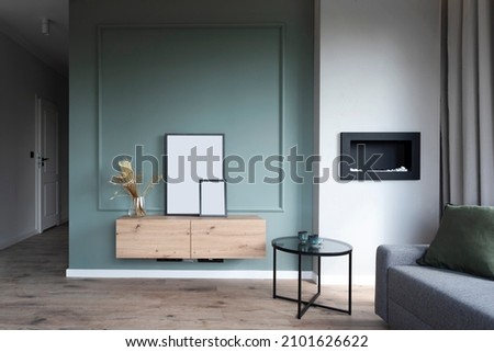 Modern interior of living room in studio with stylish green wall and wooden shelf with frame with mock up. Sofa and furniture in design apartment at home.