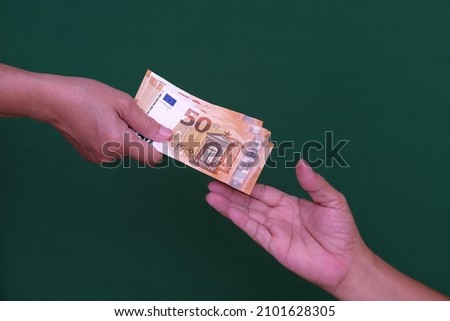 Female hand holding a few euro, male hand receiving it.