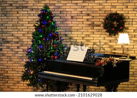 Beautiful grand piano with note sheets and Christmas tree near brick wall
