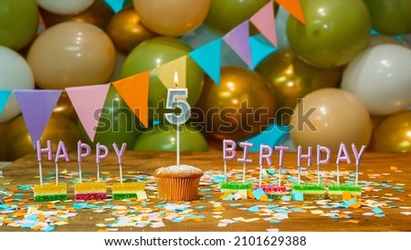 Happy birthday greeting card to 5 year old child, birthday cupcake with burning candles and birthday decorations on blue background.