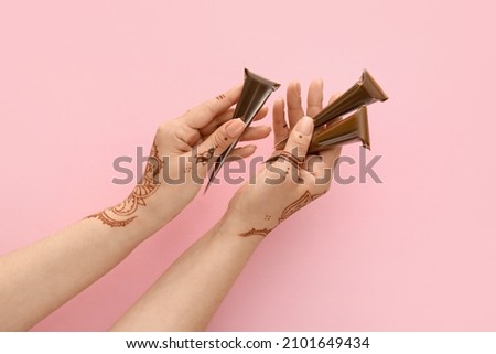 Beautiful female hands with henna tattoo and paints on pink background