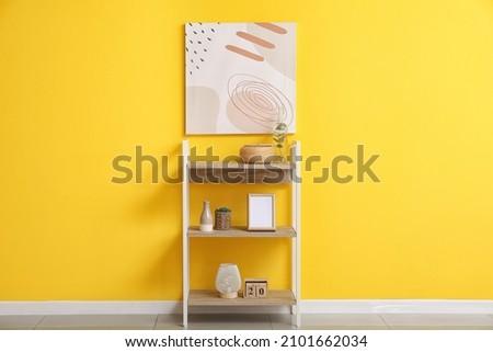 Modern shelf unit with different decor near yellow wall in room