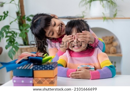 Little girl making present to little happy kid girl holding gift box,  closing eyes of cute smiling  excited with birthday surprise from her sister