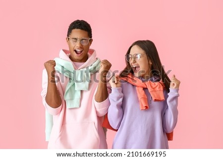 Emotional stylish young couple in hoodies on pink background