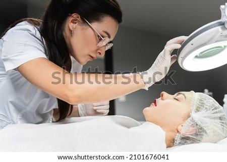 Professional permanent makeup artist and her client during lip blushing procedure Royalty-Free Stock Photo #2101676041