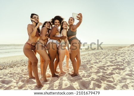 Selfie at the beach. Group of carefree young women smiling cheerfully while taking a picture together in the sun. Happy female friends having fun and making memories during summer vacation.