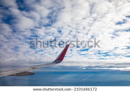 View from aircraft window, wing of an airplane flying under white clouds in the blue sky