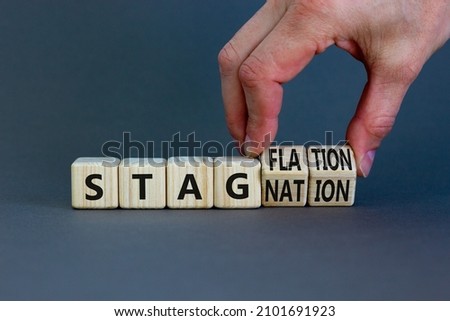 Stagflation or stagnation symbol. Businessman turns cubes, changes the word stagnation to stagflation. Beautiful grey table, grey background, copy space. Business, stagflation or stagnation concept.