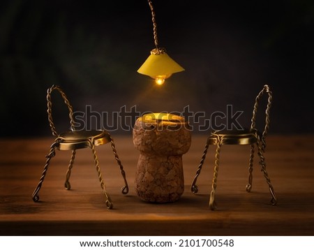 Bar mood, smoky, dark background, plank floor. The table is made of champagne cork, but the chairs are made of metal parts of cork. A yellow chandelier shines above the table. Sense photo. Mood. Royalty-Free Stock Photo #2101700548