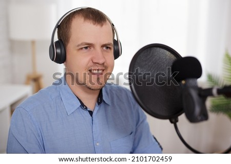 journalism, radio, podcast and blogging concept - portrait of young man talking into a microphone at the radio station