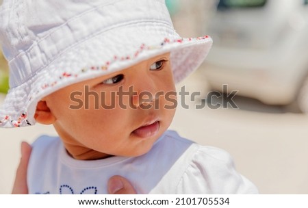 Head-shot of 6 month old baby girl wearing white floral cotton hat