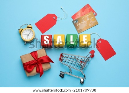 Wooden cubes with word Sale, shopping cart, gift, credit cards and alarm clock on light blue background, flat lay