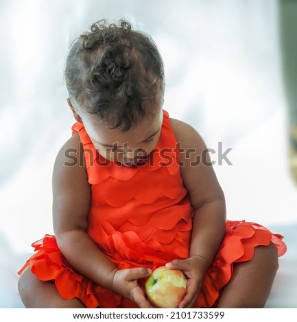 10 month old baby wearing silky orange dress with white studio background