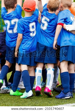 Vertical picture of happy boys in sports team celebrating success together. School kids in blue sporty jersey shirts with white numbers. Children playing sports on grass venue